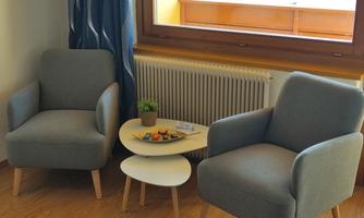 Two gray armchairs are positioned next to a small table. On the table is a plant and some sweet pastries.