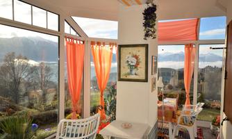 A bright conservatory with large windows and orange curtains. In the background, a beautiful landscape with mountains can be seen.