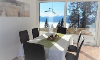 A bright dining area with a table and black chairs. Through the window, you can see a beautiful landscape with trees and mountains.