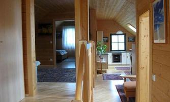 A bright, modern wooden house with an open living area. The furnishings are cozy and inviting, with a view of the kitchen and the bedroom.