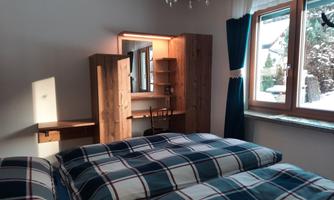 A cozy bedroom with two beds and checkered bedspreads. The room has a window overlooking the winter landscape and a wooden wardrobe.