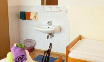 A simple room with two beds and a small sink. Colorful towels are neatly placed on a table.