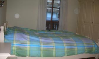 A simple bedroom with a bed covered with a striped blanket. The room has a window and a white wardrobe.