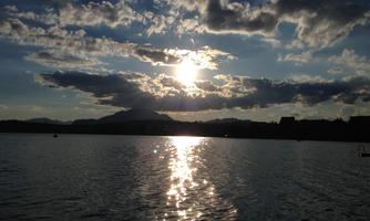 A beautiful sunset over a calm lake. The sun rays are reflecting in the water and the clouds are partially cloudy.