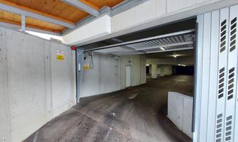 An entrance to an underground garage with a spacious interior. The walls are made of concrete and the ceiling is made of wood.