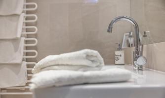 A modern bathroom with a sink and fresh white towels. In the background, towel holders and a decorative soap dispenser are visible.