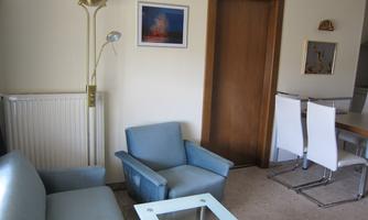 A bright living room with blue furniture and a glass table. A door leads to another room, and a picture hangs on the wall.