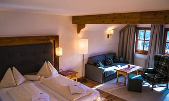 A comfortable bedroom with a large bed and a cozy seating area. Natural light flows in through the windows, creating a warm atmosphere.