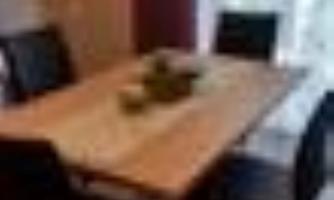 A modern wooden dining table with black chairs. A decorative bowl is on the table.
