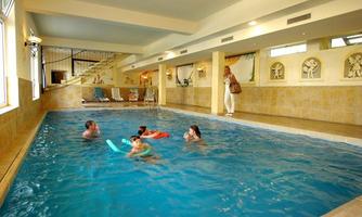 An indoor pool with clear water, where people swim and play. In the background, there are loungers and decorative walls.