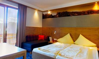 A modern room with a double bed and yellow pillows. There is a cozy seating area and plenty of daylight through the large window.