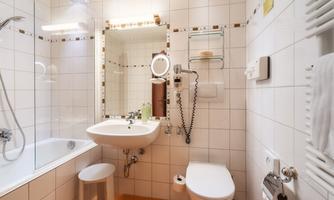 A modern bathroom with tiles and a shower. There is a sink, a toilet, and a large mirror.