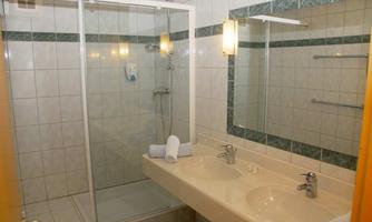 A modern bathroom with a shower cabin and two sinks. It is bright and clean with tiled walls.