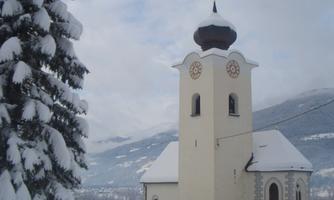 A church in the snow with a tall bell tower and a golden dome. Surrounded by snow-covered trees and a winter landscape.