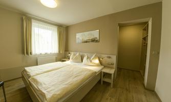 A bright and modern bedroom with a double bed and large windows. The room has a simple, friendly decor and a wardrobe in the alcove.