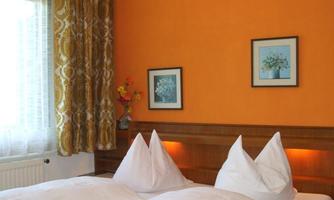 A cozy bedroom with an orange wall. Two beds with blankets and decorative pictures on the wall.
