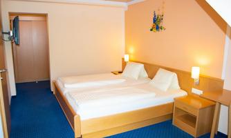 A simple guest room with two single beds and blue carpet. The walls are painted in a warm tone and there is a small nightstand as well as a dresser.