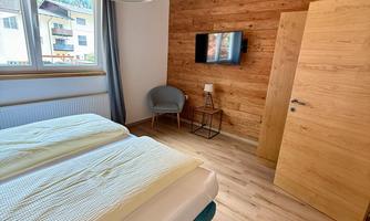 A cozy bedroom with wooden panels and a large window. It features a bed, a television, and a seating area.