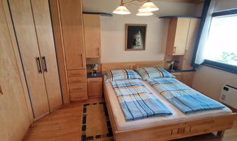A cozy bedroom with a double bed and light wooden wardrobes. The bedding is blue striped, and there is a wide windowsill with natural light.