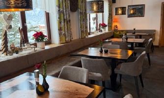 A cozy restaurant with wooden tables and chairs. The windows are decorated with flowers, creating an inviting atmosphere.