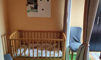 A cozy children's room with a wooden children's bed and a blue chair. The walls are painted in a warm tone.