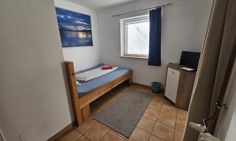A simple room with a bed, a small table, and a television. The window lets in plenty of daylight.