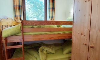 A cozy room with a bunk bed and green bedding. The window offers a view of a beautiful garden.