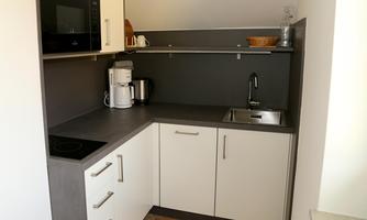 A modern kitchen with a clear work surface and modern appliances. It includes a cooking pot, a coffee machine, and a kettle.