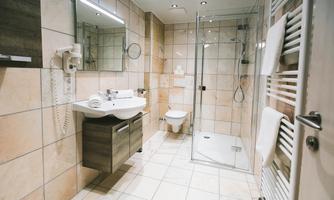 A modern bathroom with a shower, a sink, and a toilet. The walls are tiled and the room feels bright and inviting.