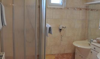 A modern bathroom with a shower cubicle, a sink, and a small stool. The walls are brightly tiled and the light is pleasant.