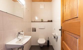 A modern bathroom with white tiles and a wooden washbasin. The decor is minimalist and bright.