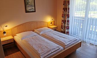 A bright bedroom with two beds and wooden details. Large windows provide plenty of daylight and a view outside.