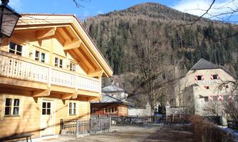 A traditional wooden house in a picturesque mountain landscape. In the background, trees and a wooded slope can be seen.