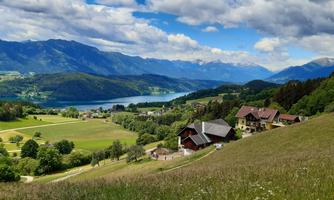 A picturesque landscape with green meadows and a tranquil lake. In the background rise majestic mountains beneath a clear sky.