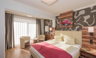 A modern hotel room with a large bed and striking wall decoration. The room is bright and welcoming, with a view of the window and comfortable seating.