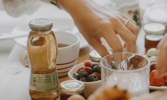 A set table with breakfast items. A hand reaches for fresh fruits and drinks.