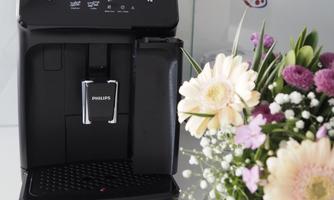An elegant coffee machine in black stands next to a colorful floral arrangement. The machine has modern controls and gives the surroundings a chic look.