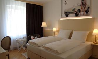 A modern hotel room with two beds and elegant furnishings. The room is bright and well-maintained, featuring a large window and a stylish piece of artwork on the wall.