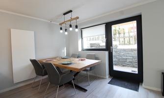 A modern dining area with a wooden table and stylish chairs. Large windows provide plenty of natural light and a view outside.