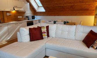 A cozy living space with a white sofa and red cushions. The open kitchen area features modern appliances and a lot of wood.