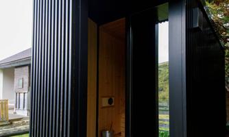 The outdoor sauna is located near the main entrance of the alpine hut and is protected by trees.