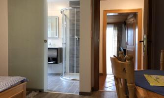 A living space with a view of a bathroom and another door. The floor is made of wood and there is a table with chairs in the foreground.