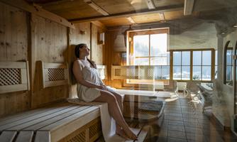 A relaxing sauna with wooden walls and plenty of daylight. A woman sits comfortably on a bench and enjoys the calm atmosphere.