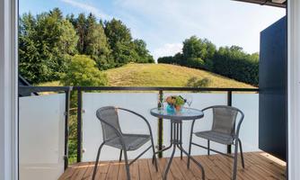 A cozy balcony with a round table and two chairs. In the background, you can see a green landscape with trees and gentle hills.