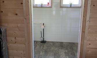 A view through an open door into a modern room with wooden paneling. The walls are brightly tiled and there are windows with small plants.