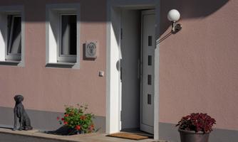An inviting entrance to a house with a light pink wall. Next to the door stands a dog statue and a blooming pot.