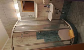Bathroom with a shower cubicle and a sink. The walls are light tiled and there is pleasant lighting.