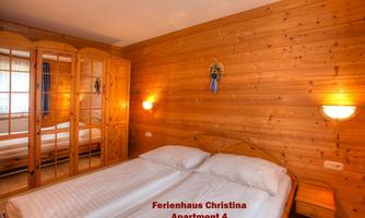 A cozy bedroom with wooden walls and a double bed. In the background, there is a mirror and a small nightstand visible.