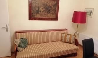 A cozy living room with a striped sofa and a red lampshade. A picture of a rural scene hangs on the wall.