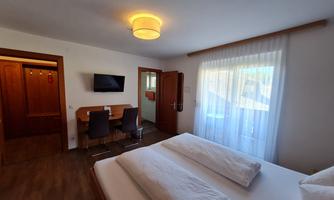 A bright and friendly hotel room with a double bed, a table, and chairs. The room features large windows that let in plenty of natural light.